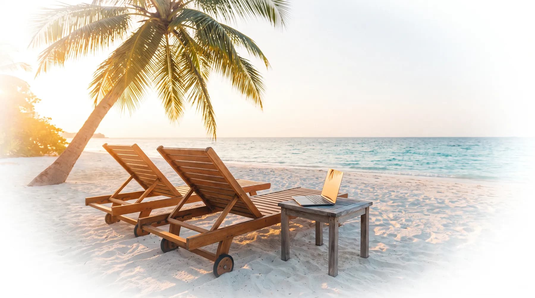 Two loungers on a beach at sunset with a laptop on a side table